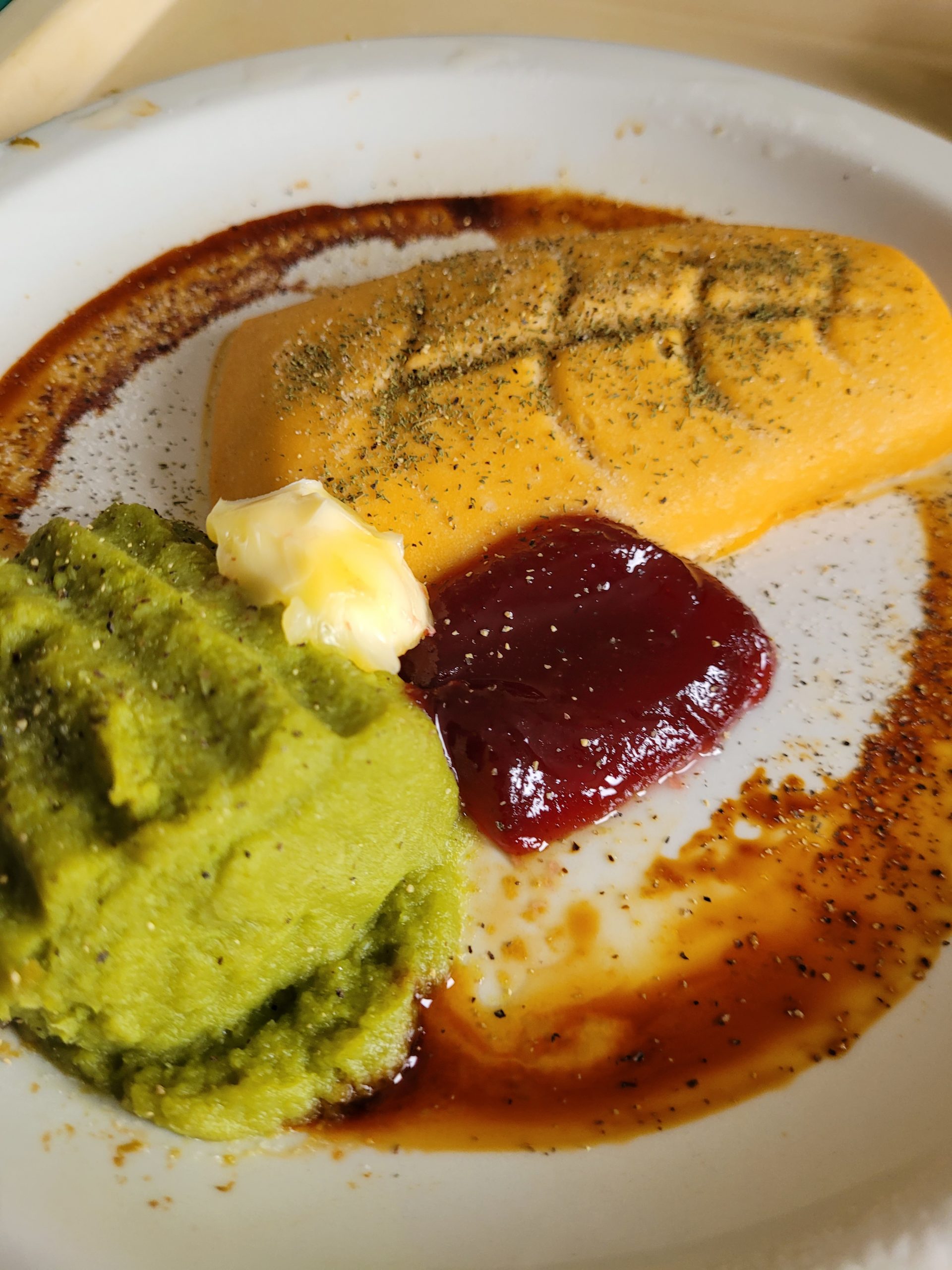 A plate with shapes of pureed fish and green beans, with cranberry jelly, a dollop of margarine, and dill on top.