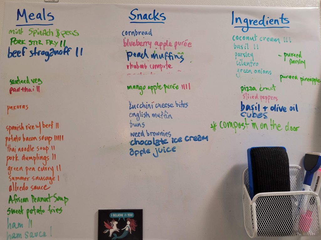 The freezer portion of a fridge/freezer with whiteboard sticker and a long list separated into meals, snacks and ingredients